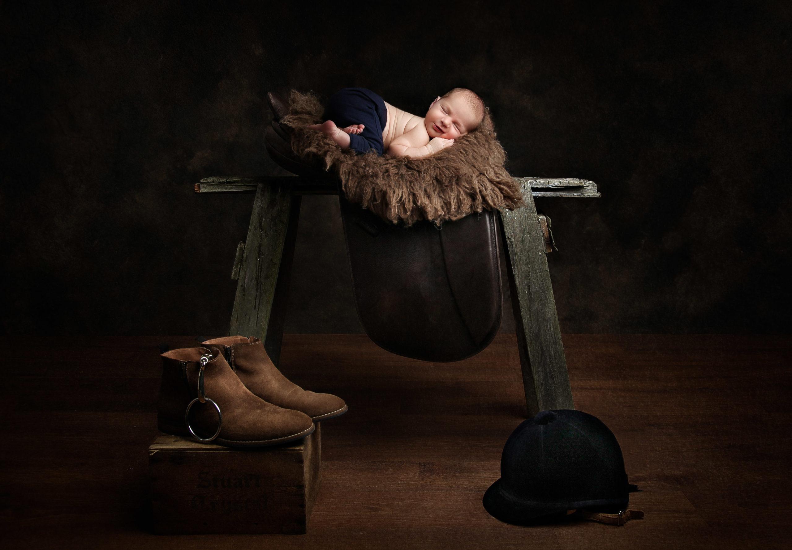 newborn baby asleep on a saddle with some riding boots on the floor