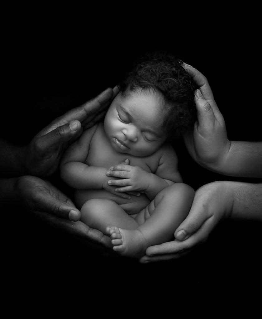 black and white image of baby with mum and dads hands