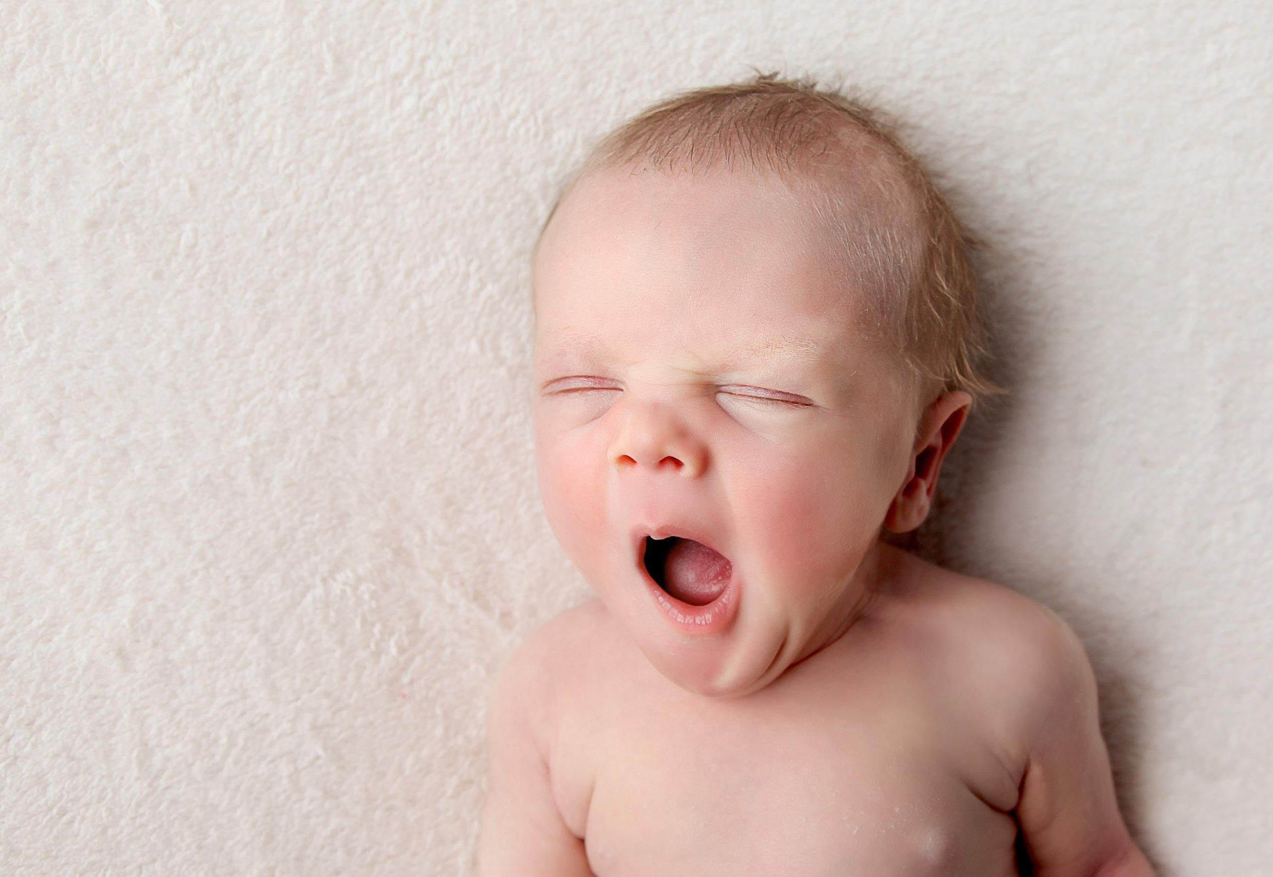 newborn baby yawning lay on a white backdrop