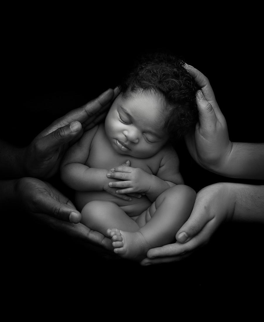newborn baby held by parents hands in black and white