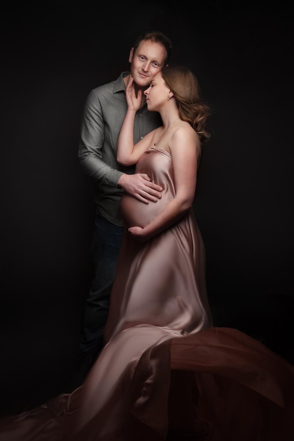 man and women in an embrace holding bump, wearing pink fabric