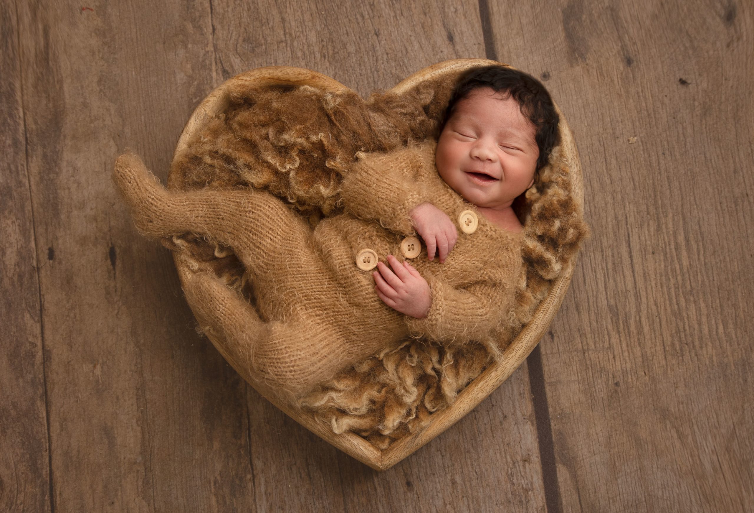 baby in a heart shaped bowl with a big smile by newborn photographer Leeds