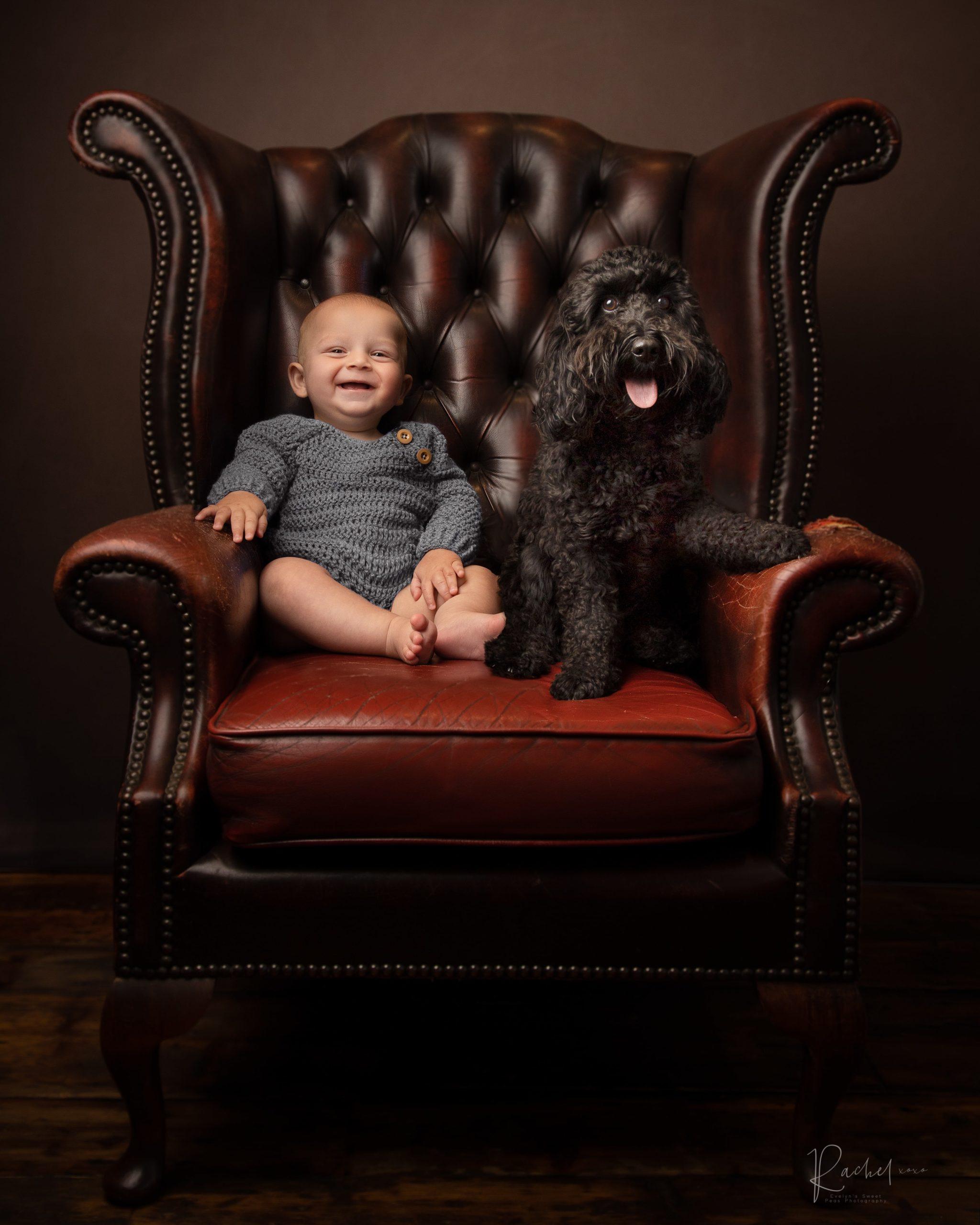 sitting baby boy on a red leather chair with a black dog, by Newborn Photographer Leeds