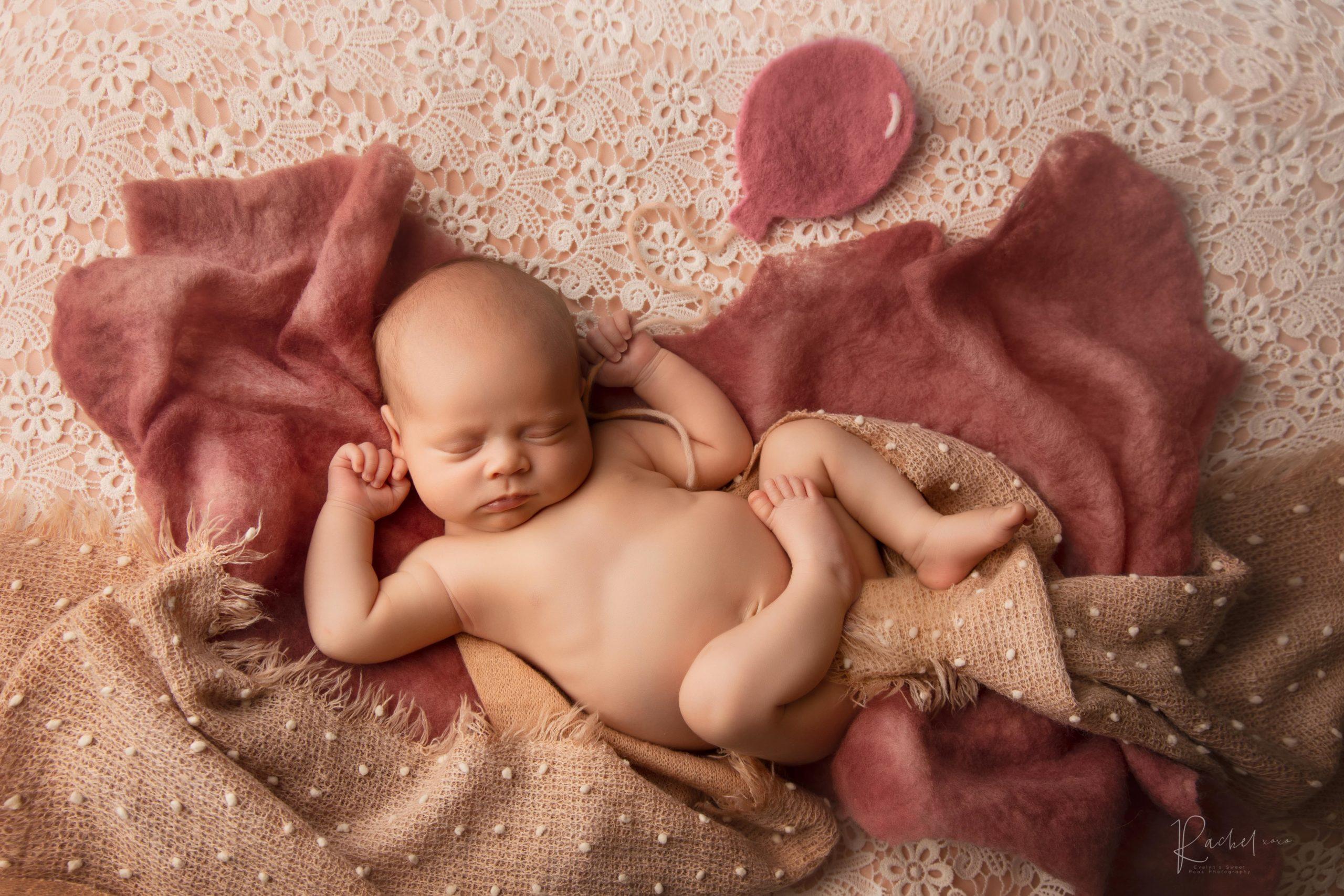 newborn baby asleep on pink layers holding a balloon 