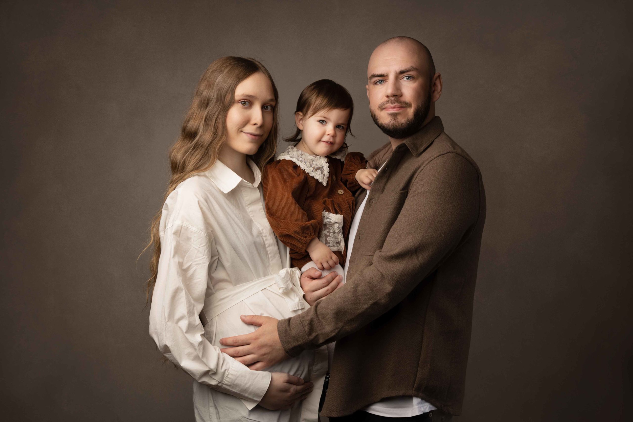 family of two parents and toddler girl wearing brown by Newborn Photographer Leeds 