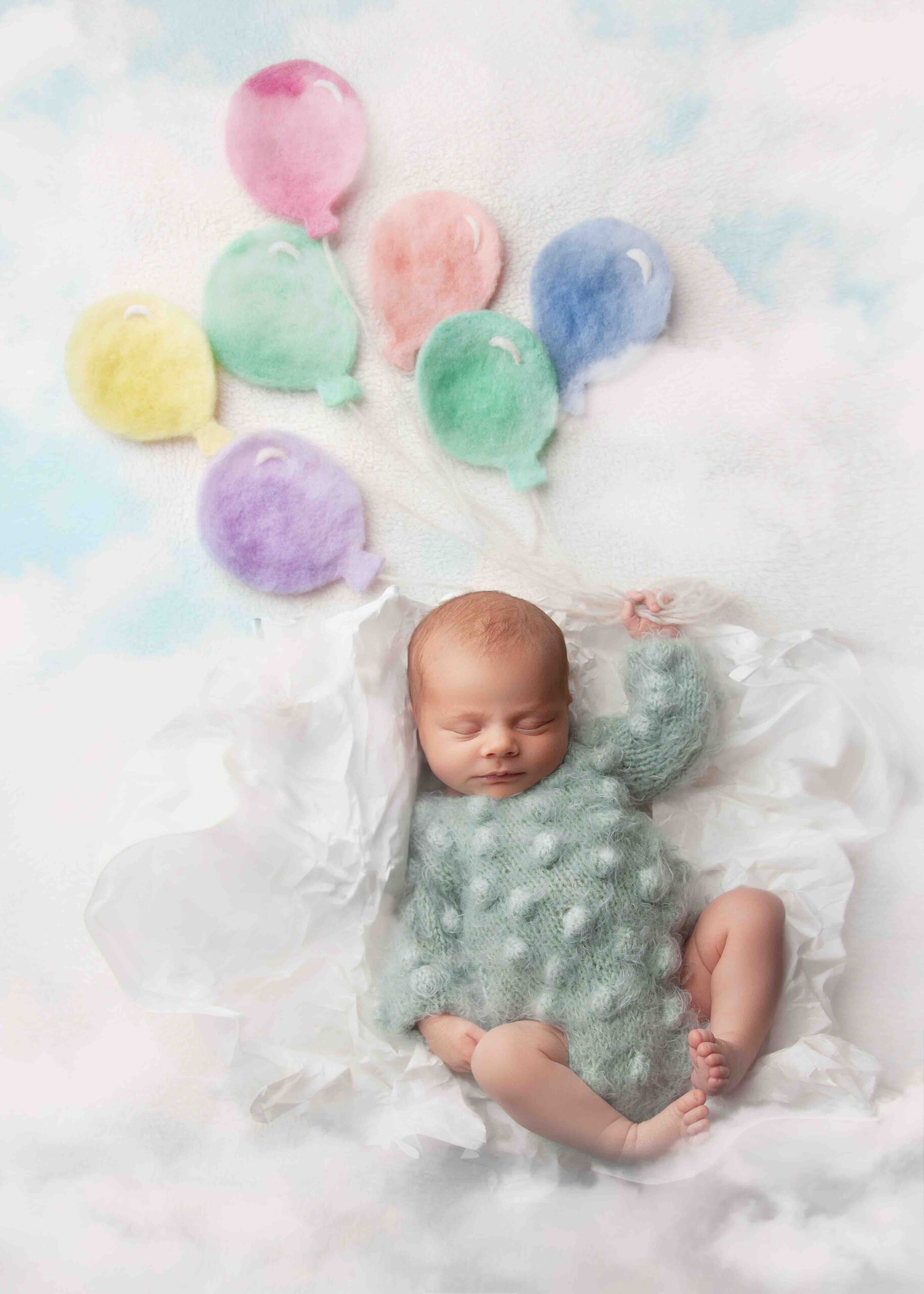 newborn baby lay on white holding balloons